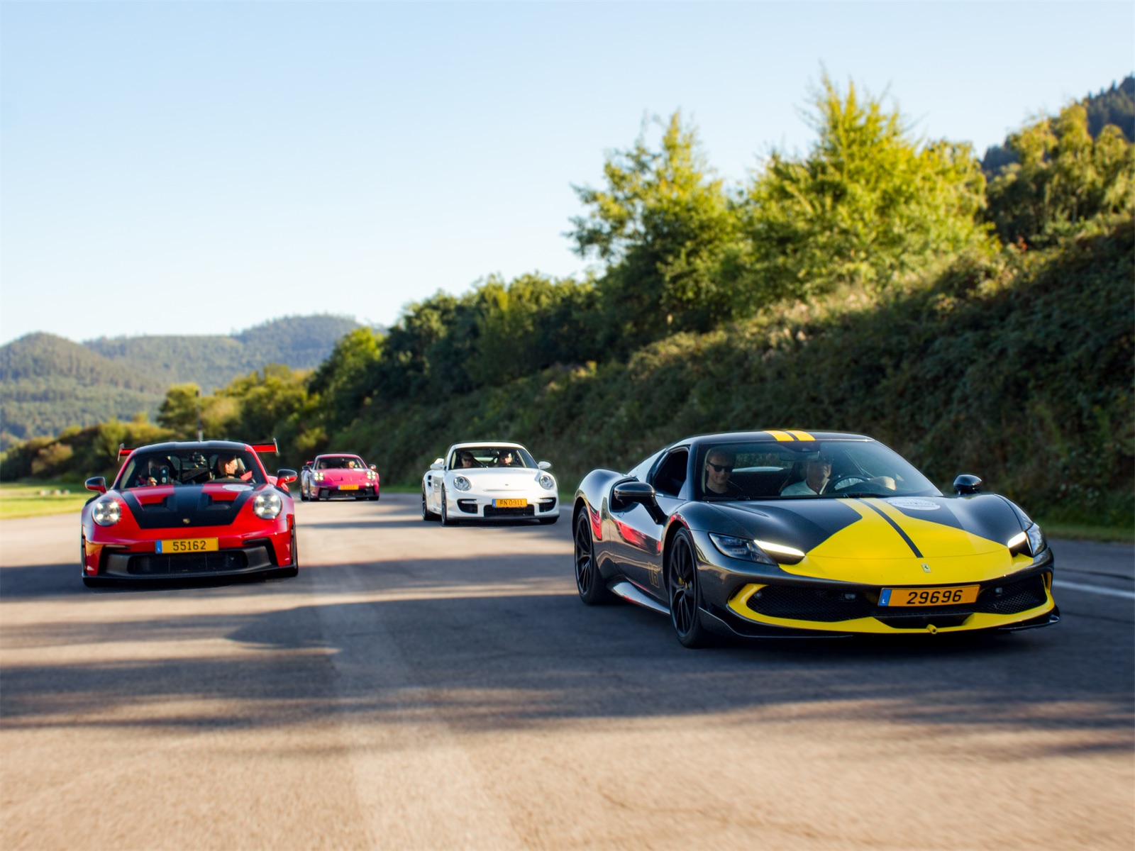Ferrari en tête d'un convoi de Porsche sur une route de montagne pendant un roadtrip