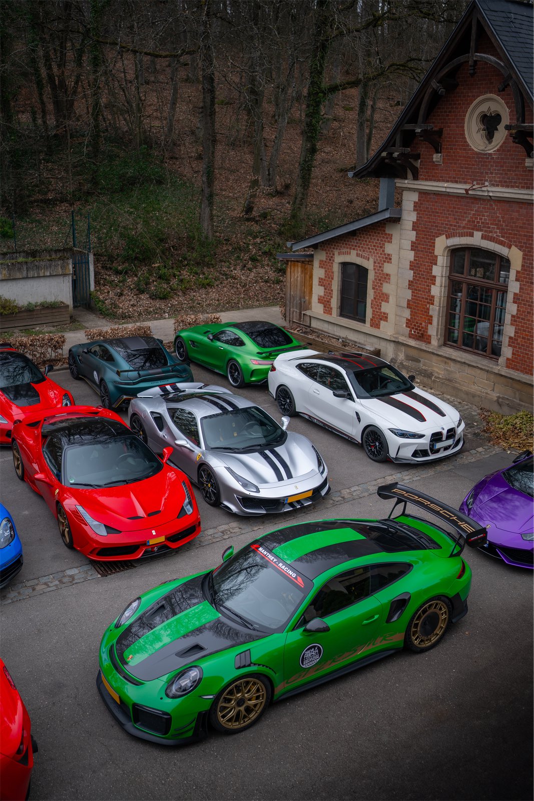 Des Porsche 911 vertes et une Ferrari garées devant un petit bâtiment de brique, en mars 2024